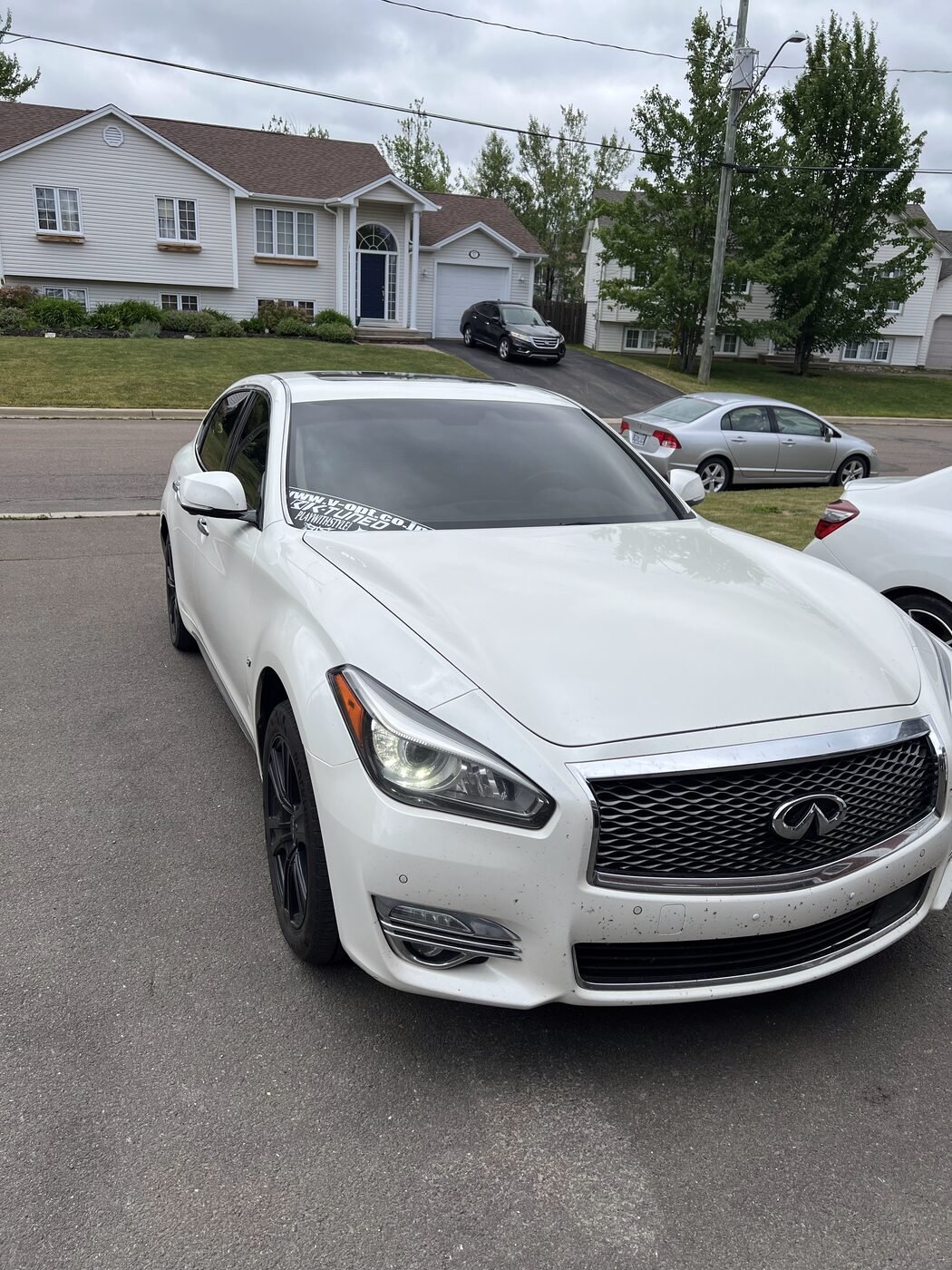 White Infiniti sedan photographed from the front on a Moncton street, its windshield clear and its side windows dark with tint